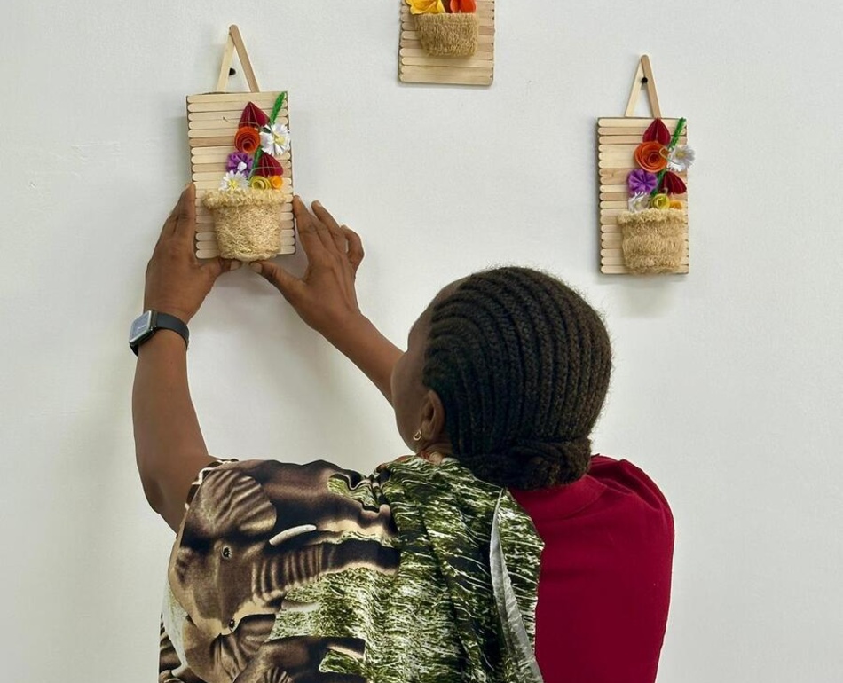 A Congolese refugee woman places her recycled art pieces on a wall at her home..