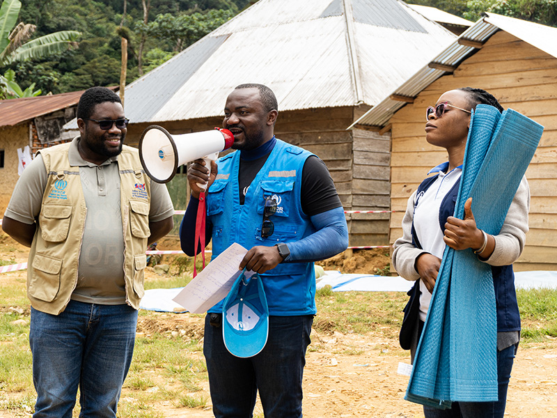 A UNHCR staff stands with a megaphone in between two other staff members of UNHCR's partner organizations