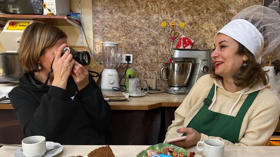 A person taking a picture of a person sitting at a table with food