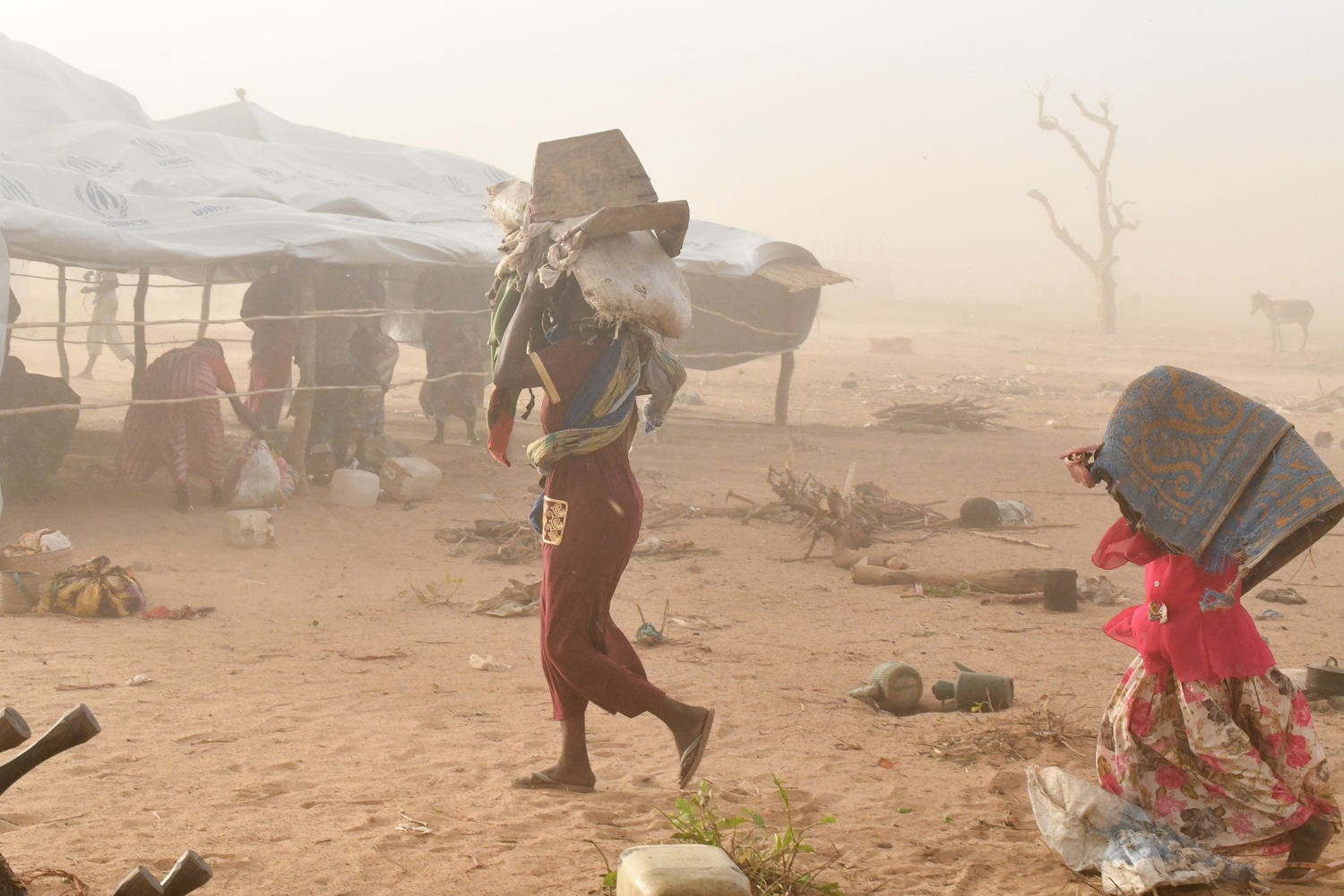 A woman and a child carry their belongings as they seek shelter during a sandstorm.