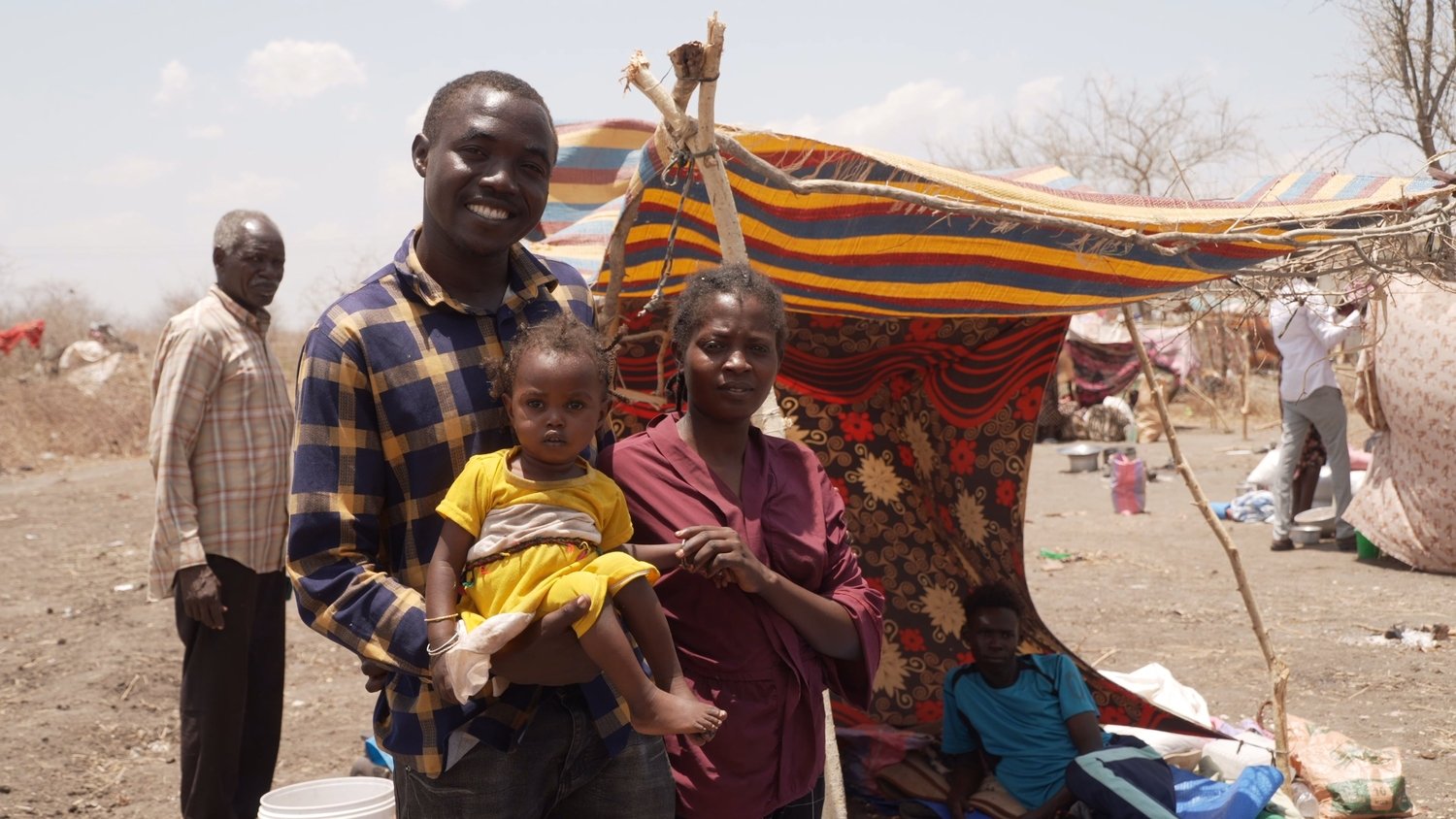 A man stands next to a woman holding a little girl in a yellow dress.