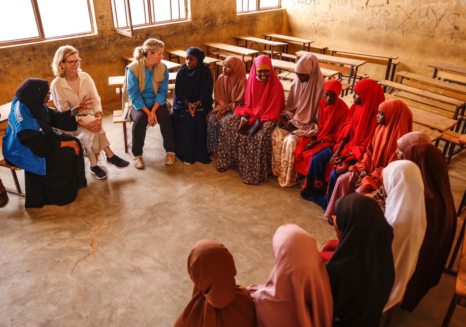 Refugee schoolgirls and staff from international organizations sit in a classroom.