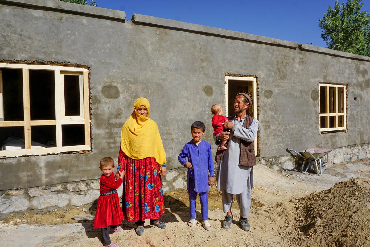 A man holding his child stands with his wife and two children in front of a newly built apartment.
