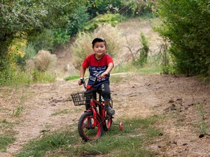 A young boy in a red t-shirt sits on his bike.