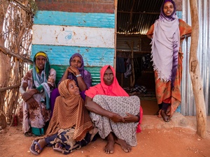 A group of women sit and stand outside a shelter.
