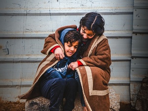 A young Syrian refugee wraps herself and her younger brother in a blanket as they sit outside in the cold in the Zaatari refugee camp.