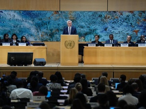 A man in a suit speaks at a lectern in a conference room