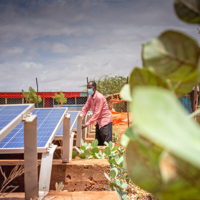 A man stands next to a solar panel farm. 