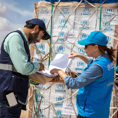 Two UNHCR staff members check a shipment of emergency supplies against a list