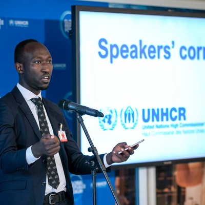 A man gives a speech, behind him a sign reads ' Speakers' Corner'