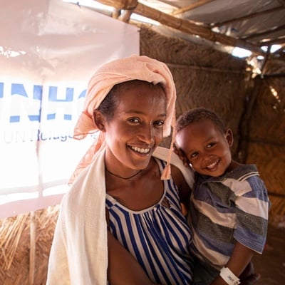 A mother holds her young son inside a UNHCR shelter. Both smile for the camera.