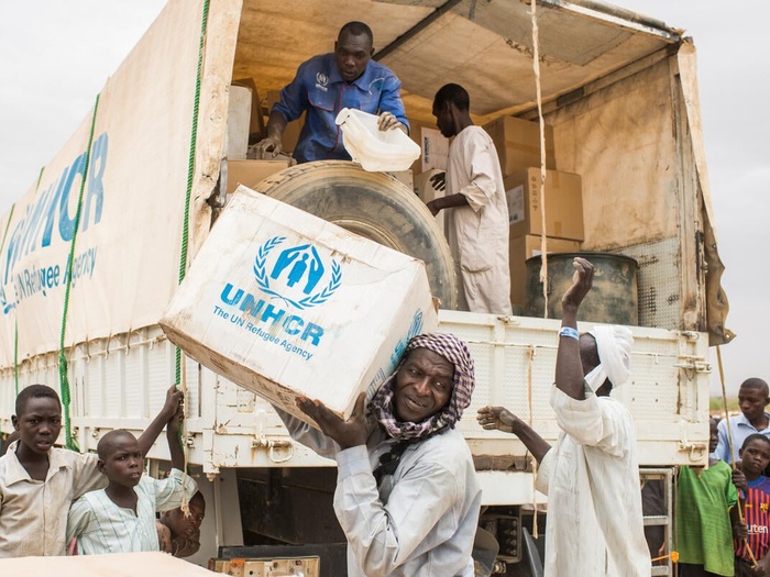 UNHCR staff unload boxes of emergency supplies from a truck in a refugee camp. 