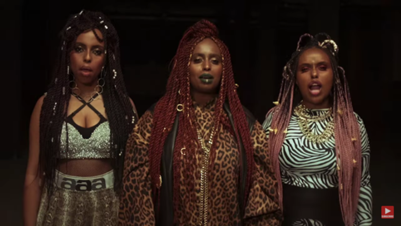 Image from a music video; three women are looking at the camera and singing