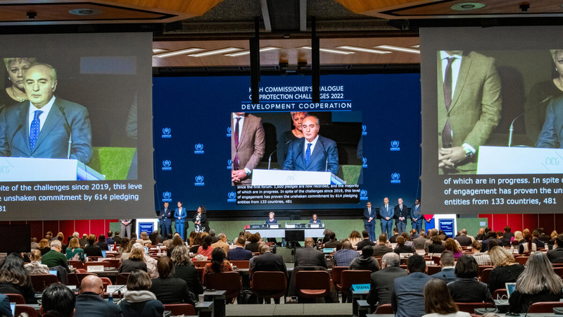Three large screens show a projection of a speaker in a huge conference room.