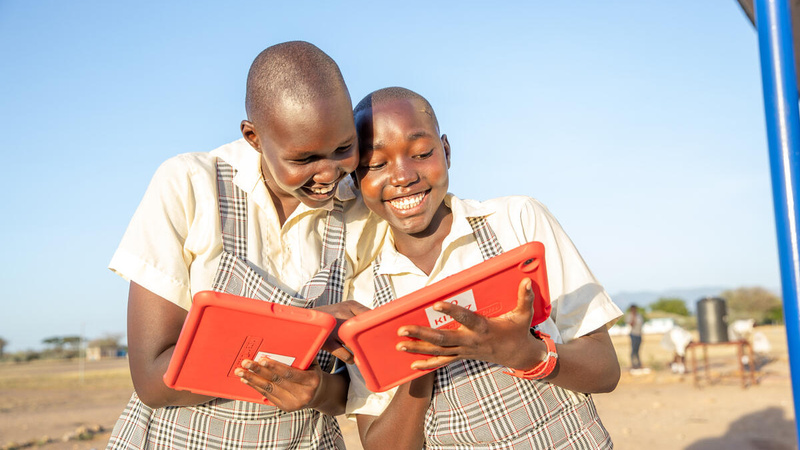Two girls smiling as they use bright orange tablets.