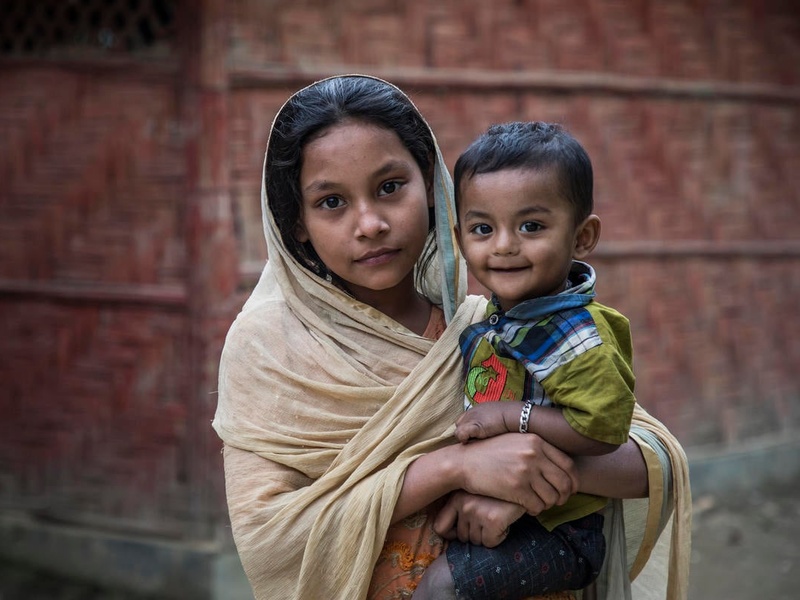 A young Rohingya girl holds her little brother