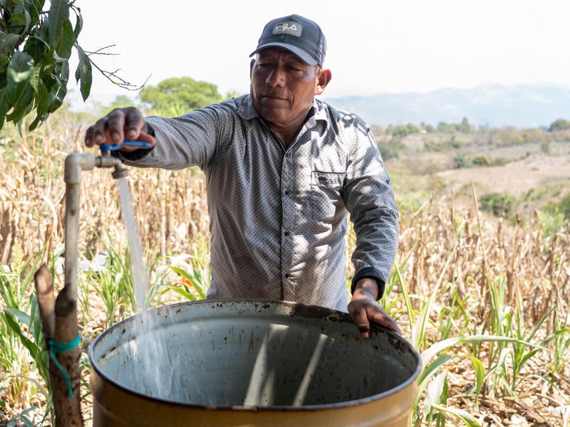Salvadoran farmer José fills a metal drum with water on his farm.