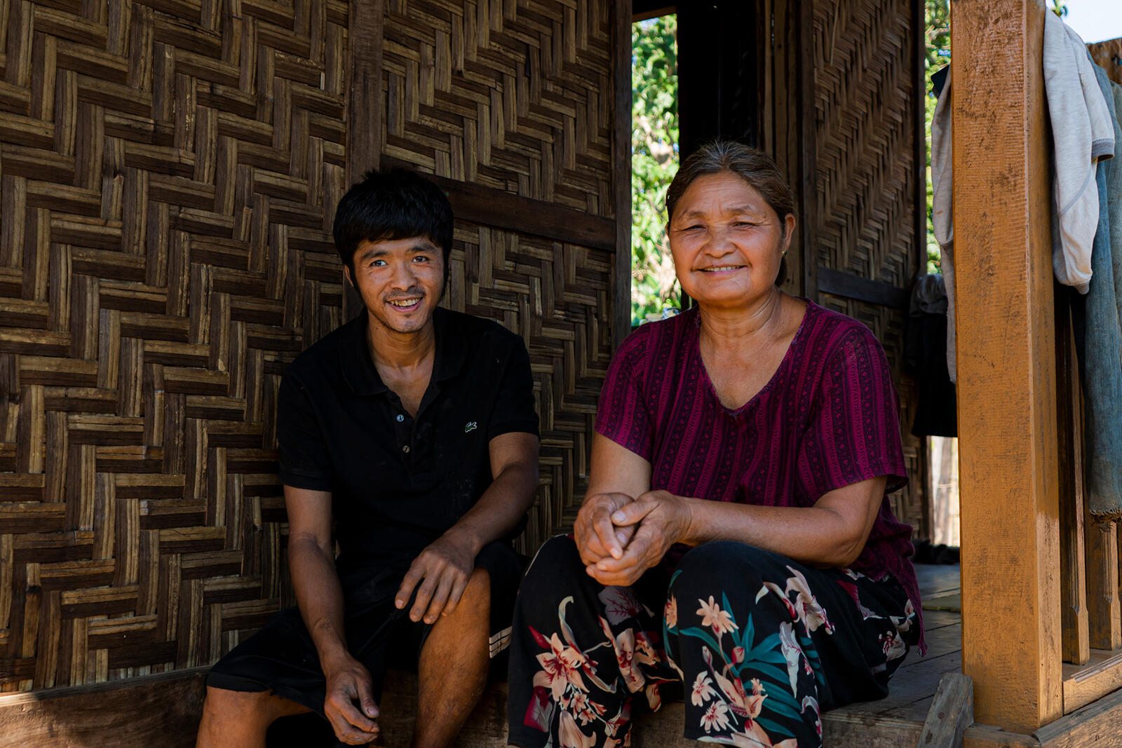 Udi Doi Ra, 56, sits and smiles with her son in a wooden house.