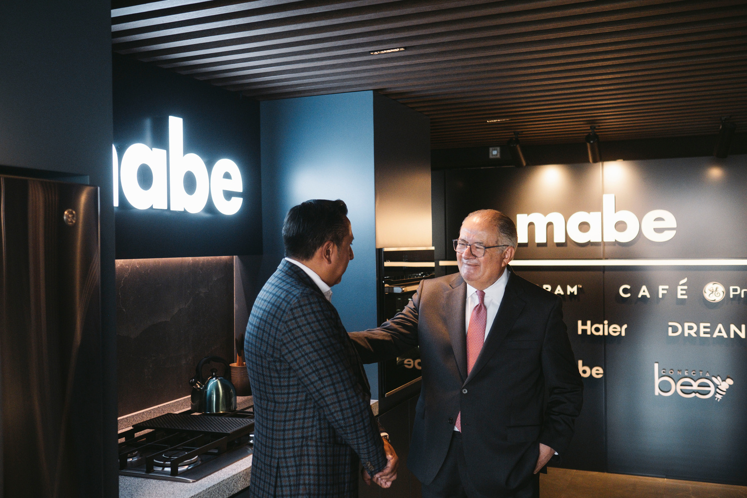 Two men wearing suits greet each other in a kitchen showroom