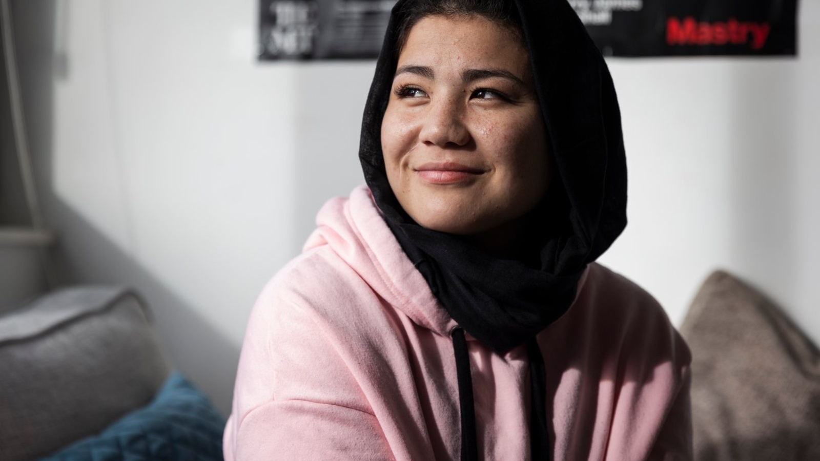 A young smiling woman in a pink hoodie and a black head scarf.