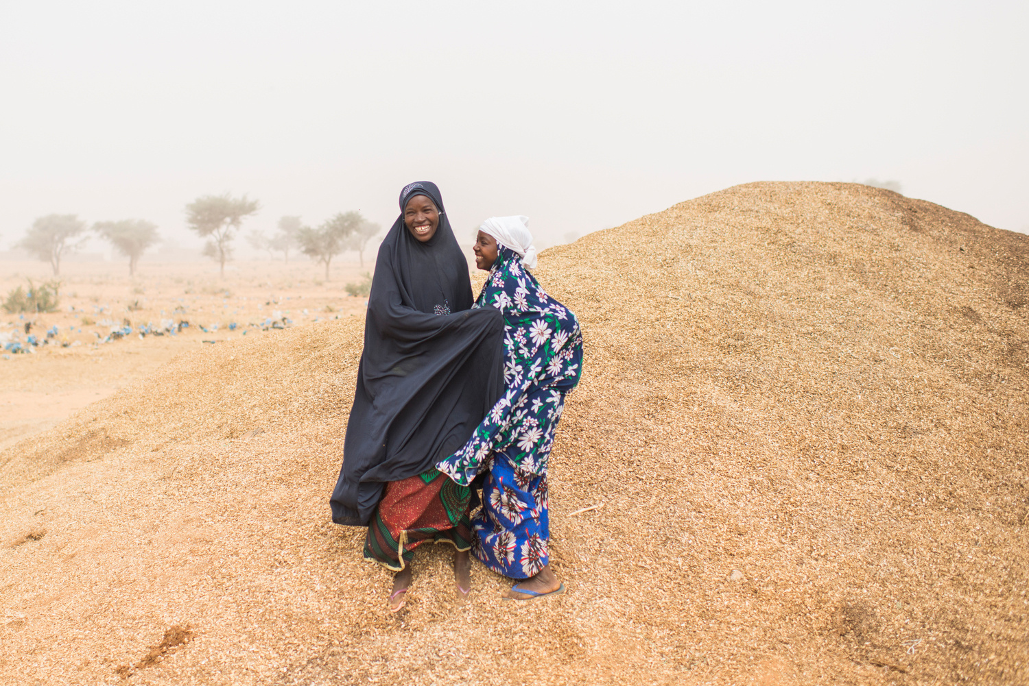 Two women stand on small hill laughing together.