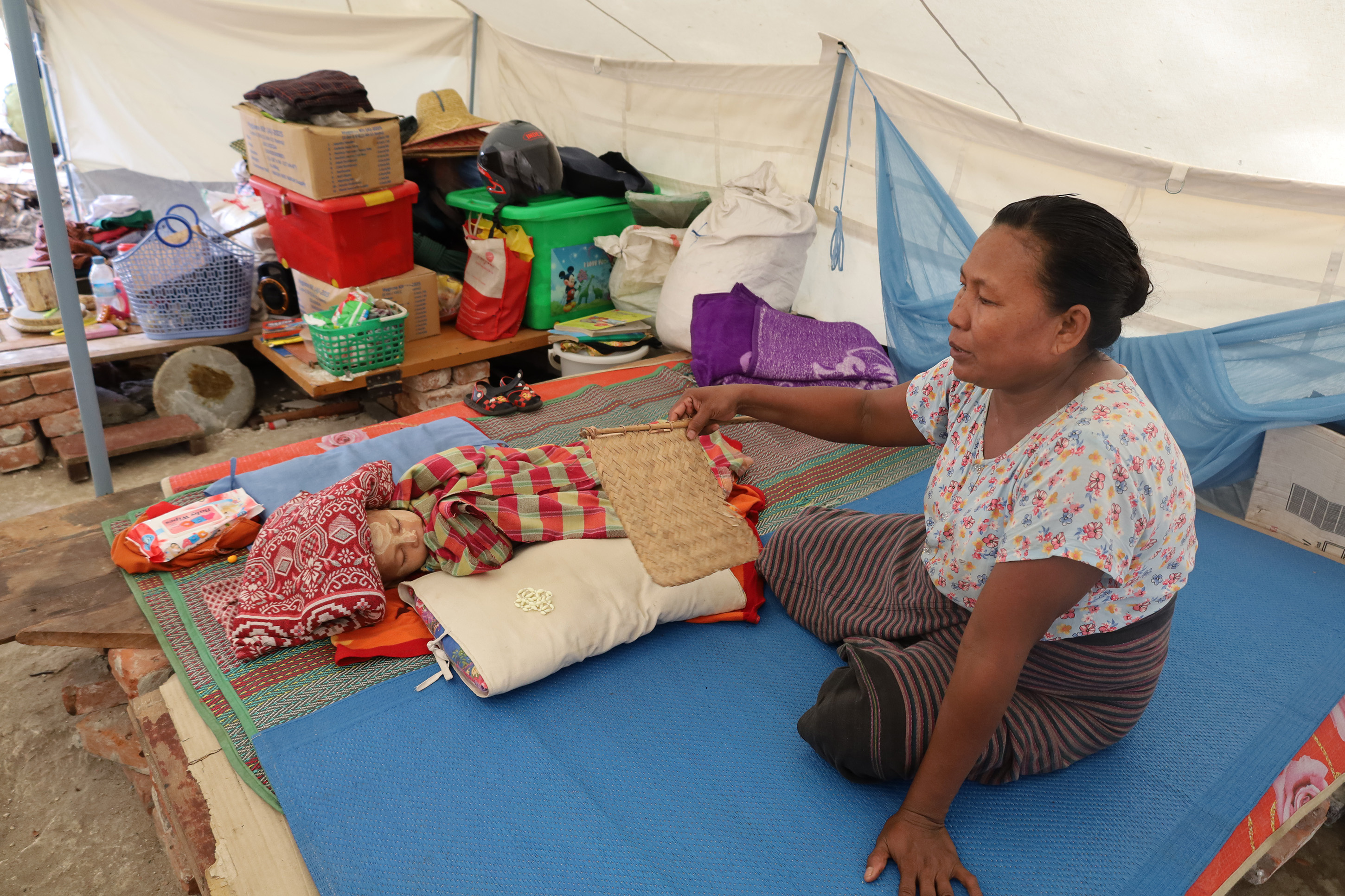 Daw Swe Win fans her baby to sleep inside the family tent where they are now living after the earthquake