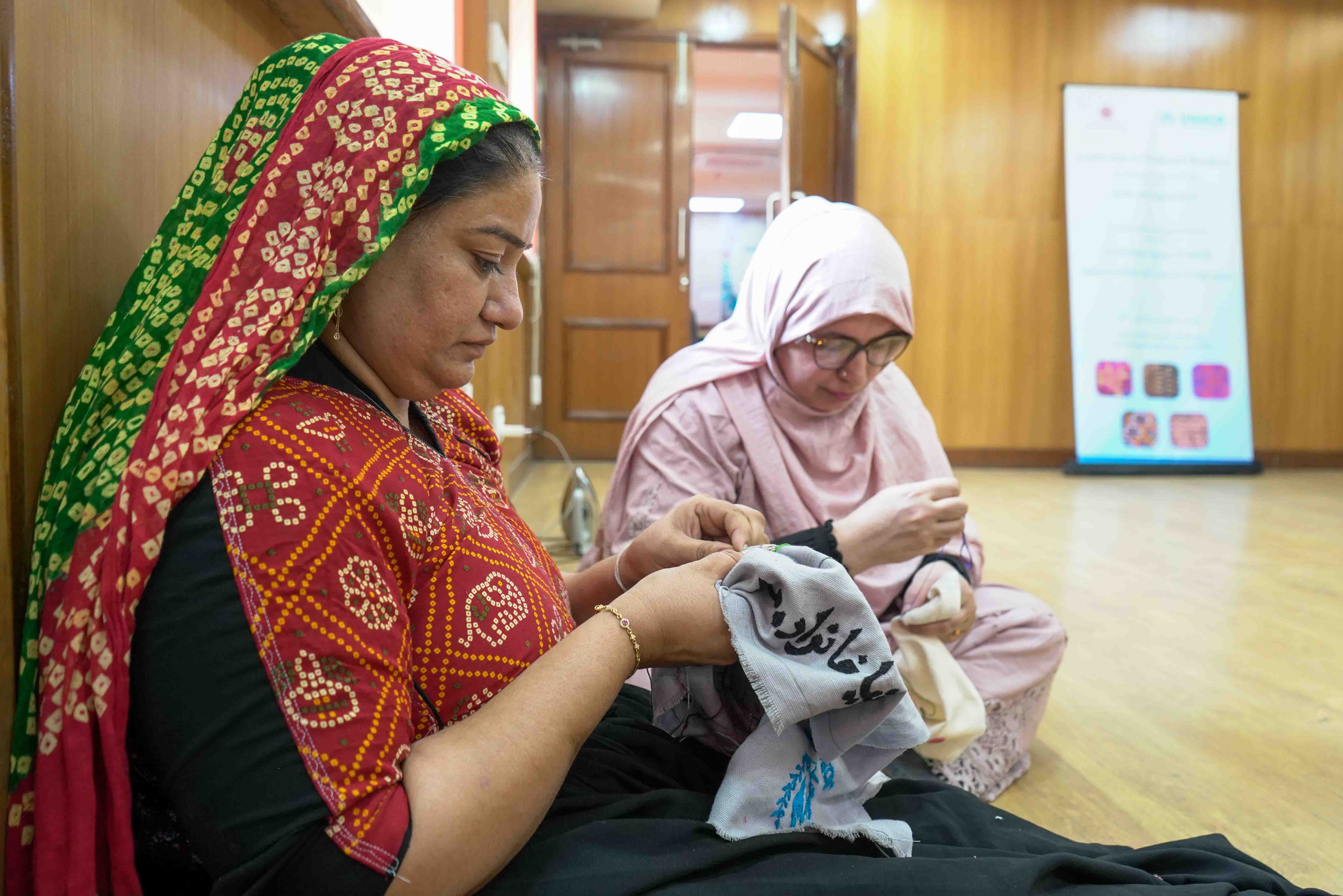 Dharmila Ahir and Khalida Mahmodi co-create a joint embroidery piece, blending Kutch and Afghan traditions.