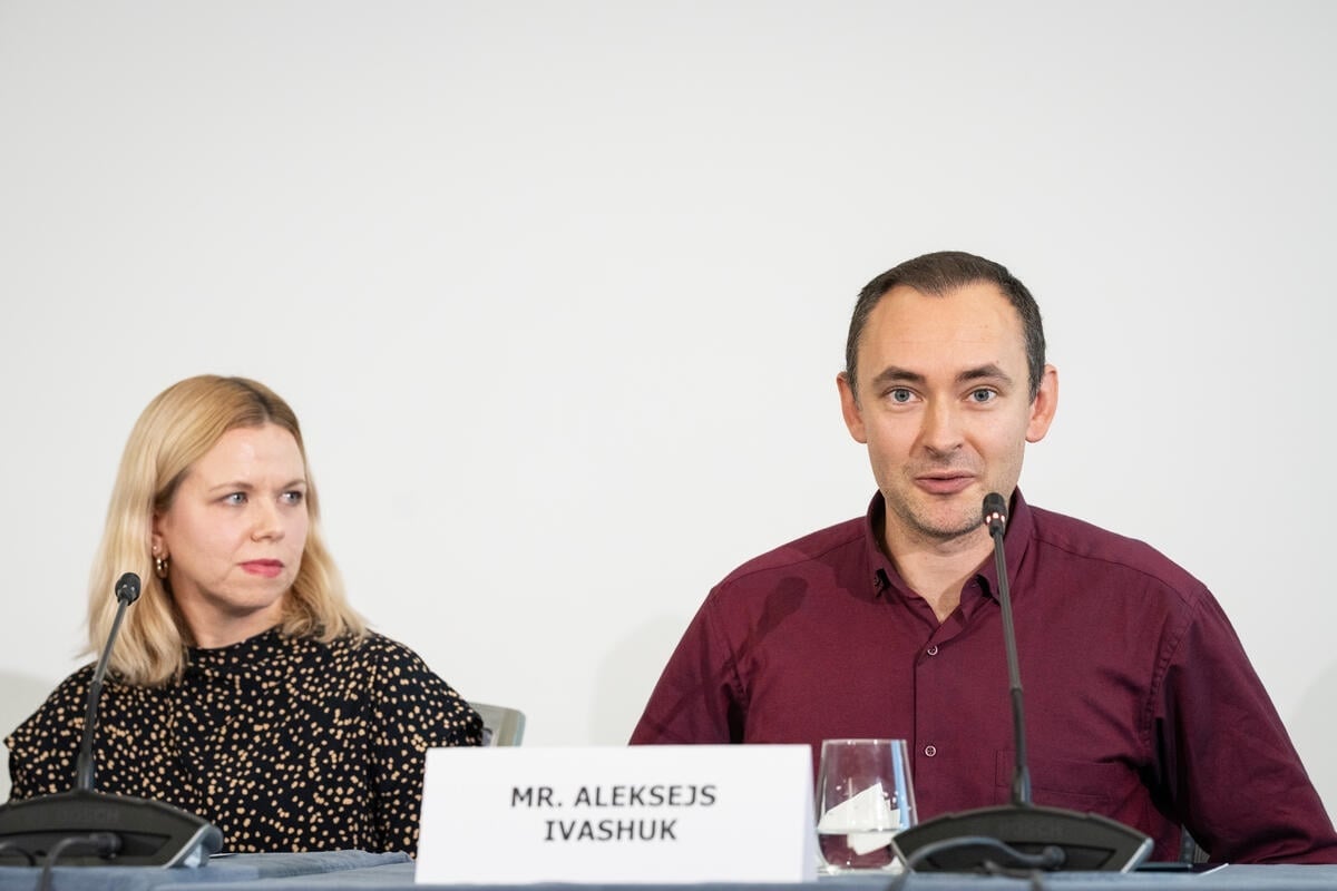 Two speakers on a panel, with the nameplace for Mr. Aleksejs Ivashuk in front of them.