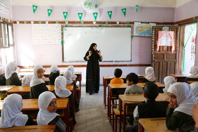 A teacher at the front of a classroom, with many students