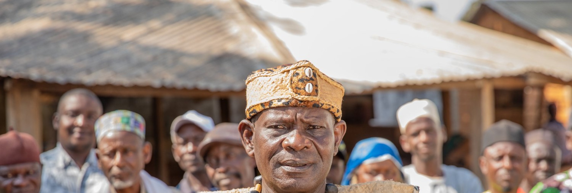 A man in colourful robes with his arms crossed stands in front of a group of people