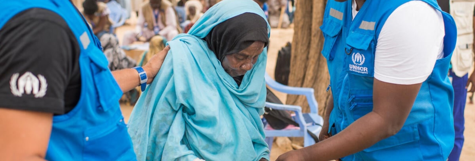 Two UNHCR staff members speak with an elderly Sudanese refugee woman. 