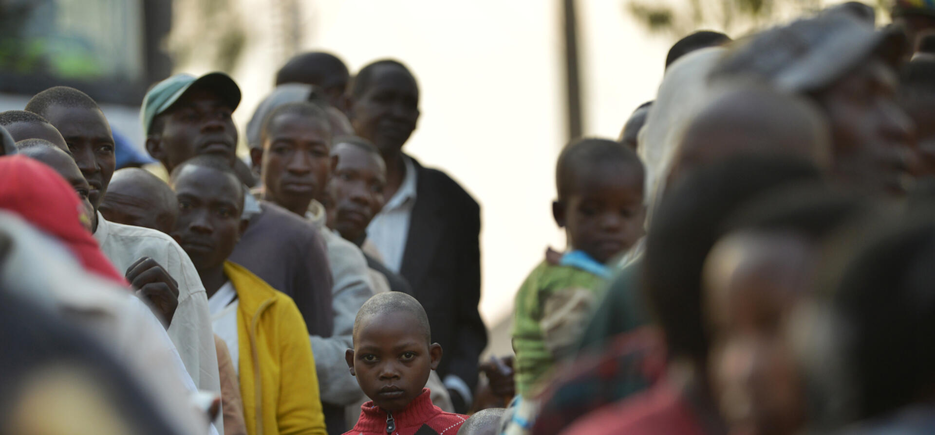A child in a crowd of people stands and looks at the camera.