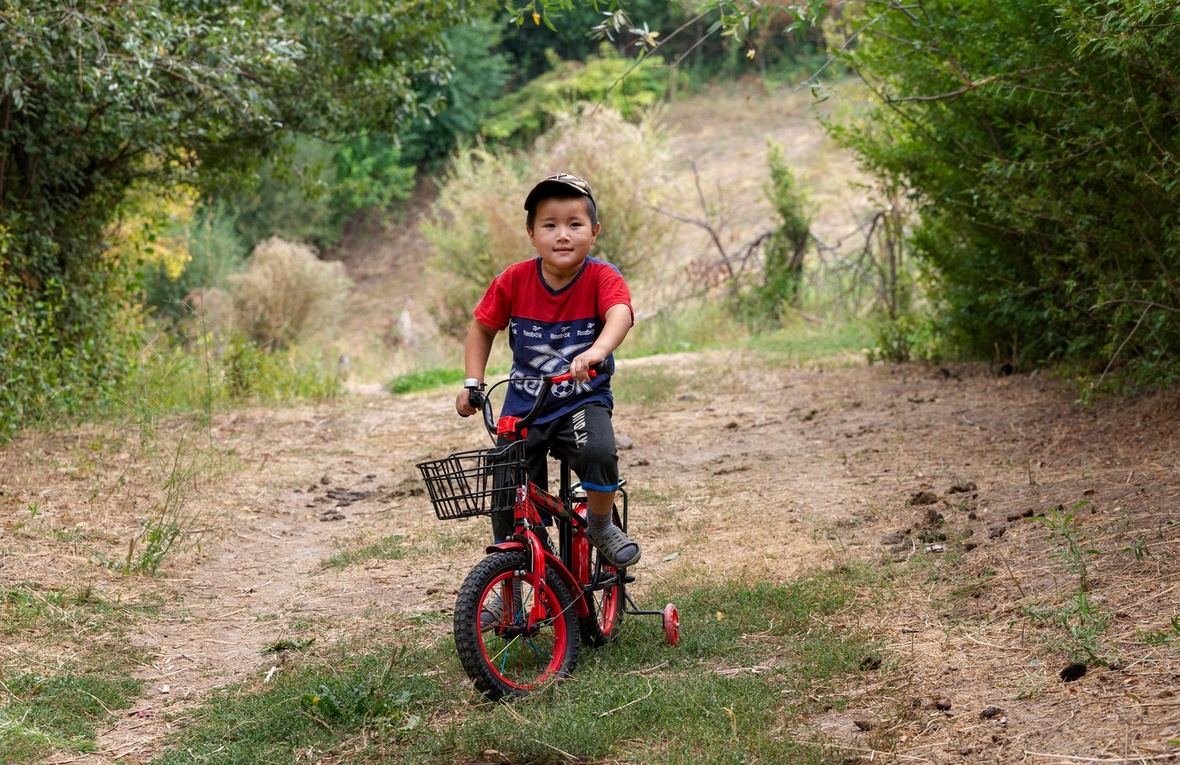 A young boy in a red t-shirt sits on his bike.