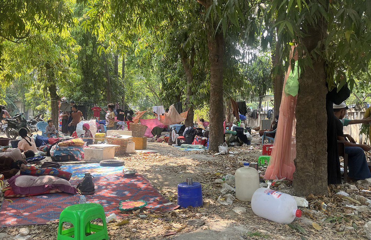 Families gather in the open under trees with their belongings.