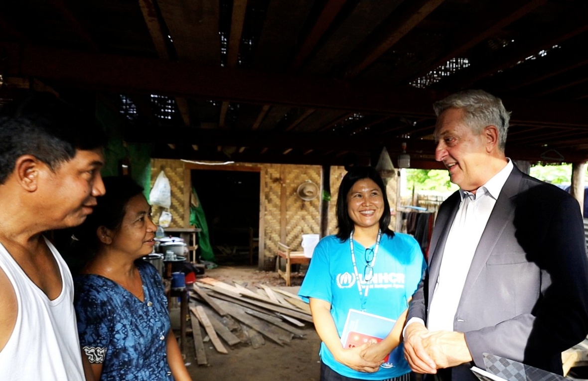 A couple speak to a man in a suit and a woman in a blue UNHCR t-shirt under a shaded area