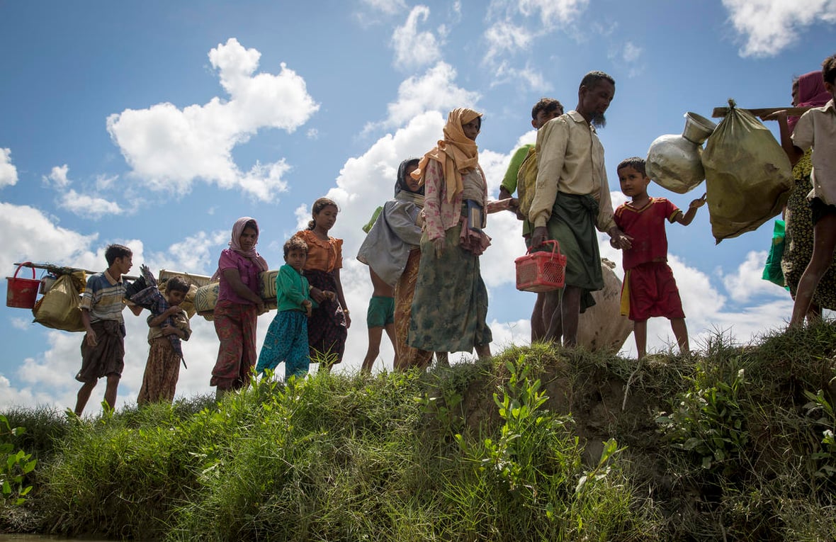 A group of Rohingya men, women and children carry their belongings across a grassy ridge