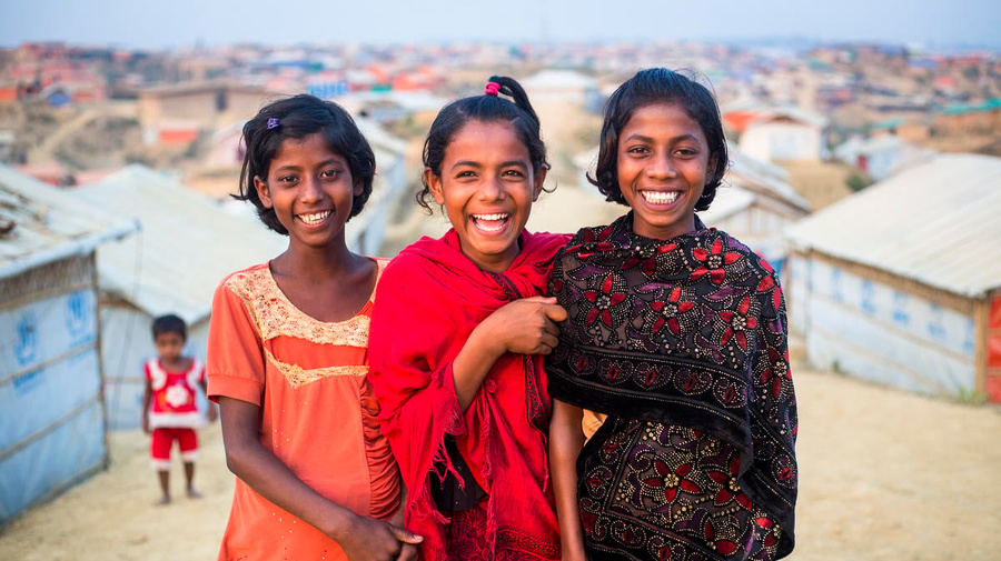 Three girls smile for the camera, in Kutupalong Refugee Camp.