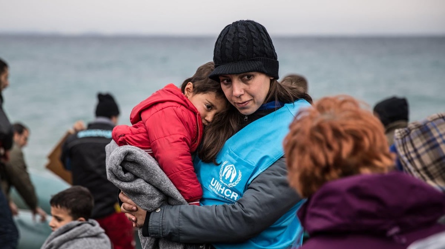 A UNHCR staff member holds a young refugee child in a blanket.