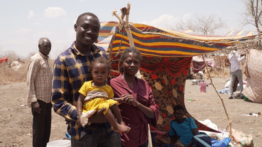 A man stands next to a woman holding a little girl in a yellow dress.