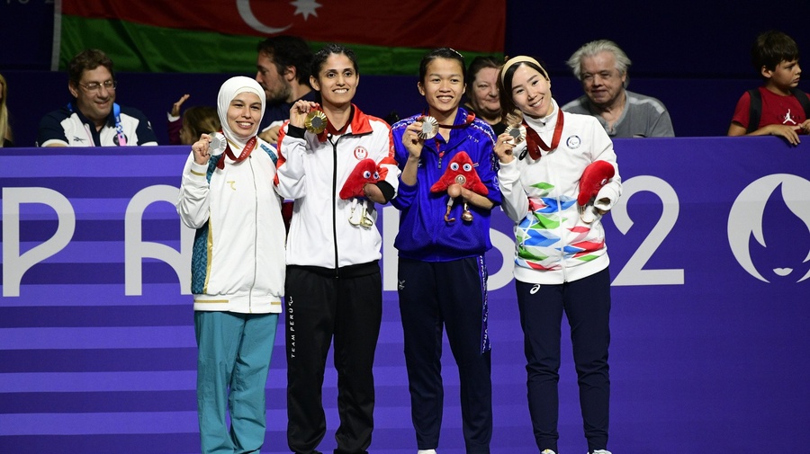 Four women stand alongside each other holding up medals around their necks.