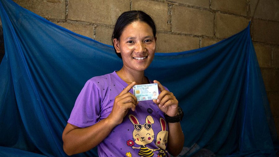 A woman holding an ID card in both hands smiles at the camera