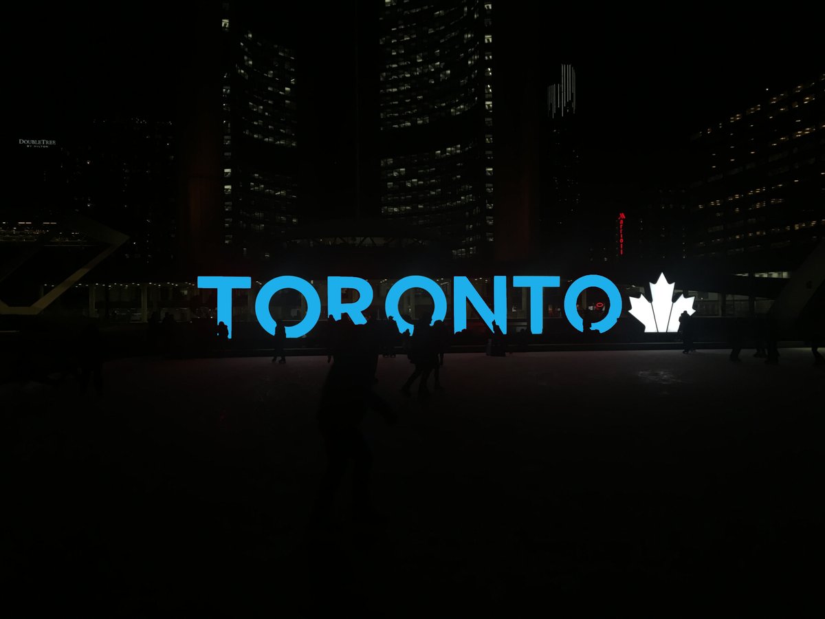 The CN Tower illuminated in  blue between two towers in downtown Toronto.