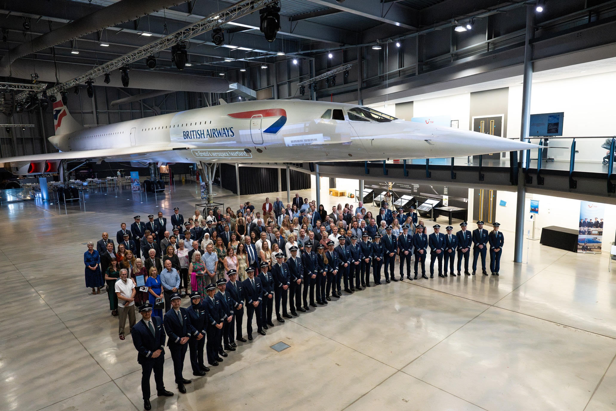 Eine Gruppe von Absolventinnen und Absolventen und ihre Familien in einer großen Halle mit Flugzeug