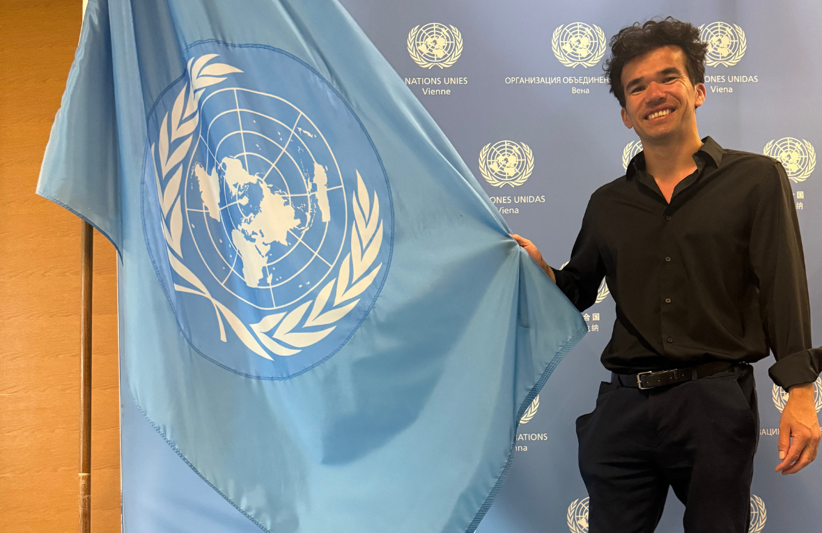 Mann neben blauer UN-Fahne l&auml;chelt in die Kamera