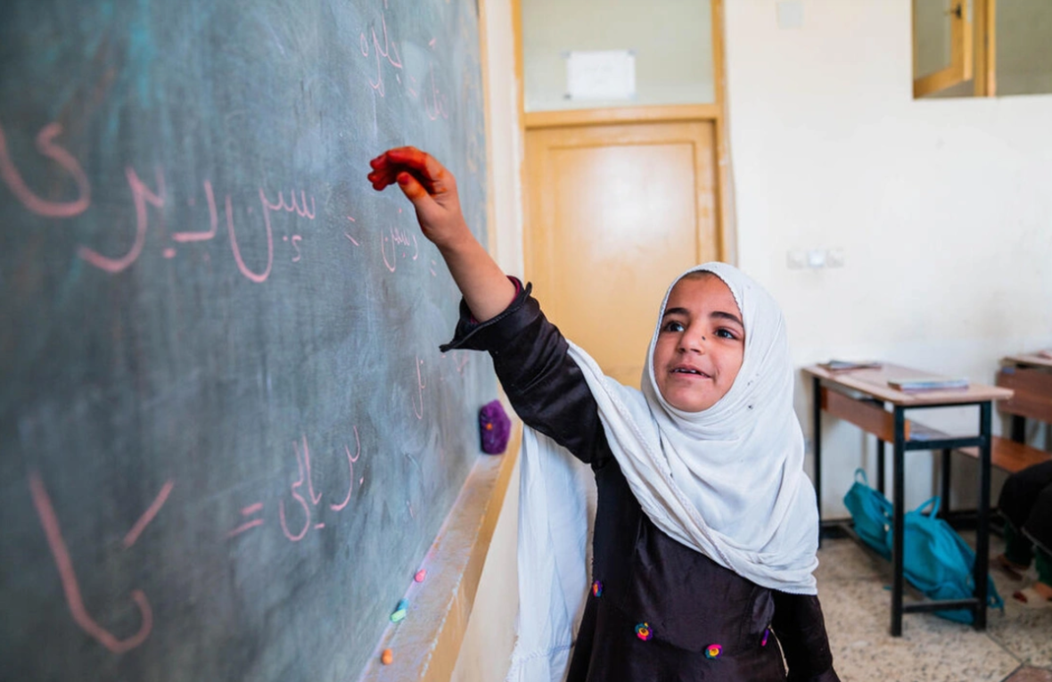 Ein kleines Mädchen in einer Grundschule in Afghanistan schreibt im Unterricht an der Tafel. 