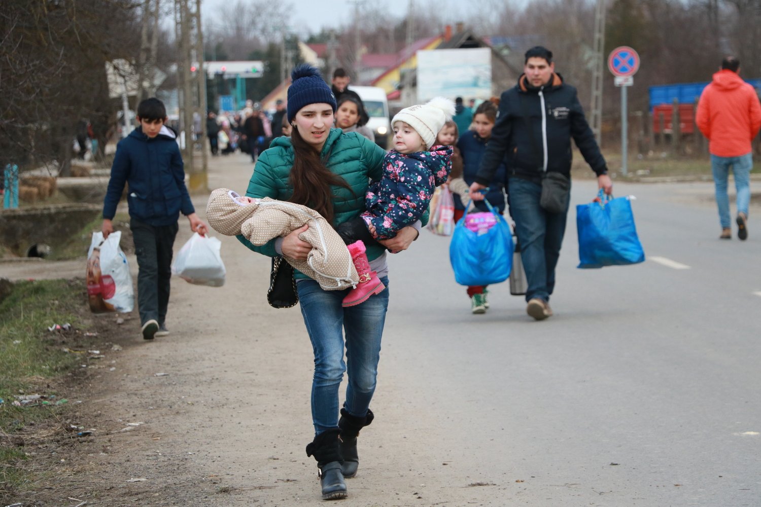 A woman hurries down a road carrying her baby on one arm and a toddler in the other.