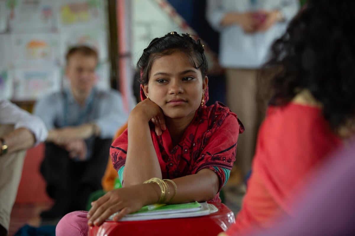 A girl dressed in red looks away from the camera while leaning on a small pile of books