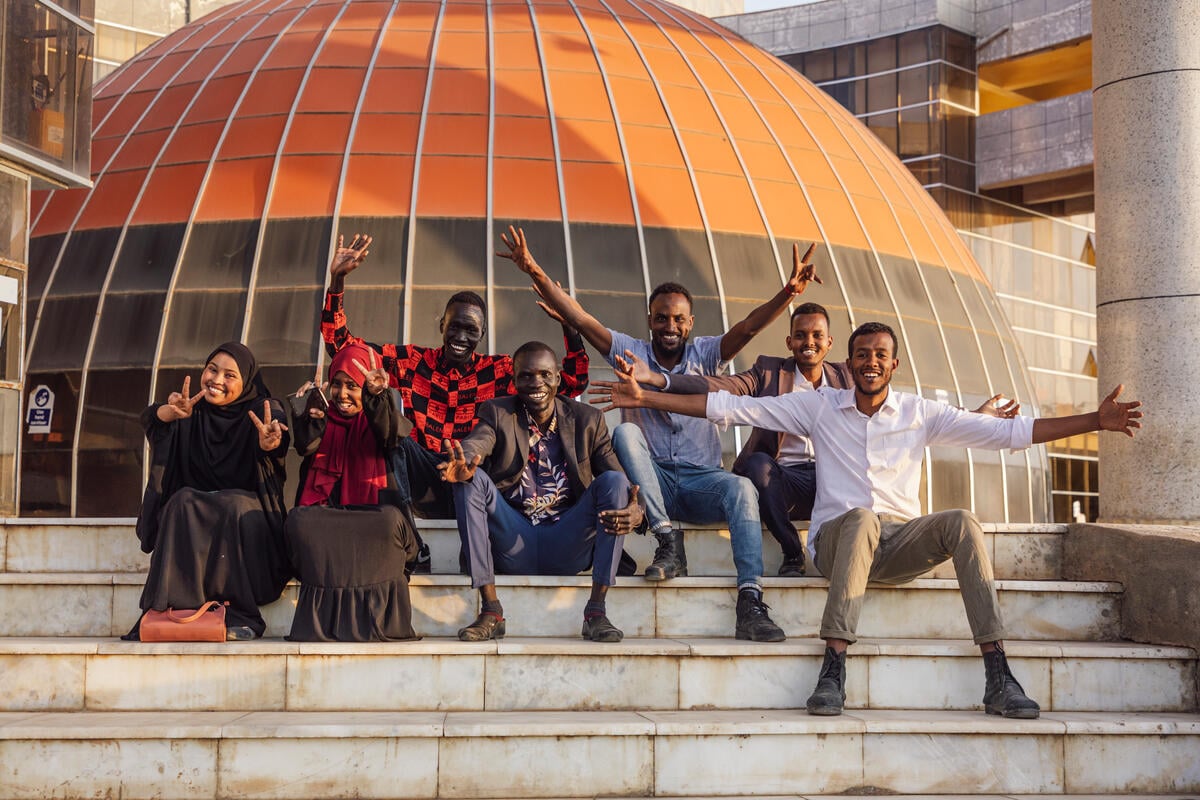 A group of young women and men, sitting on the stairs in front of their university.