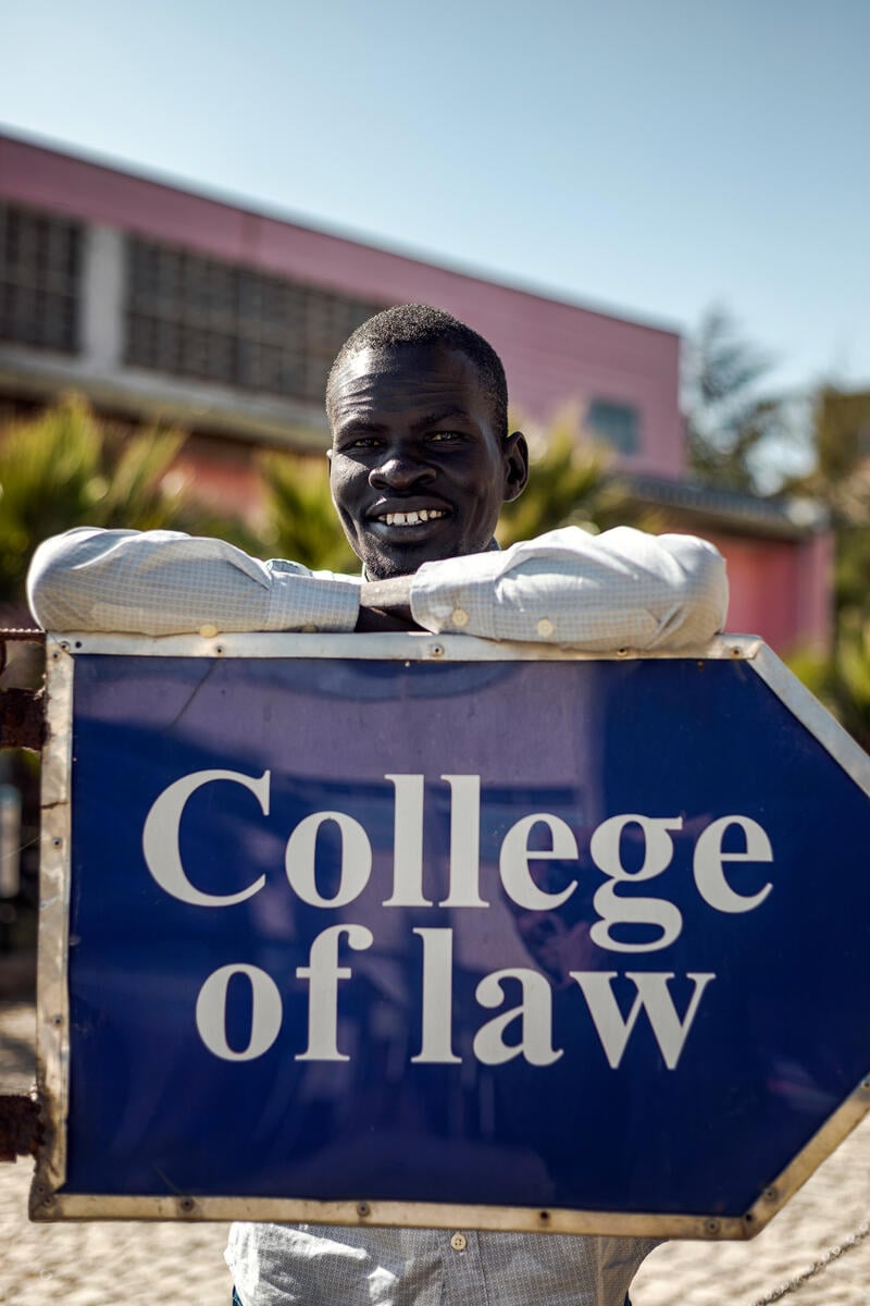 A young man poses, leaning against a sign that reads "College of law"