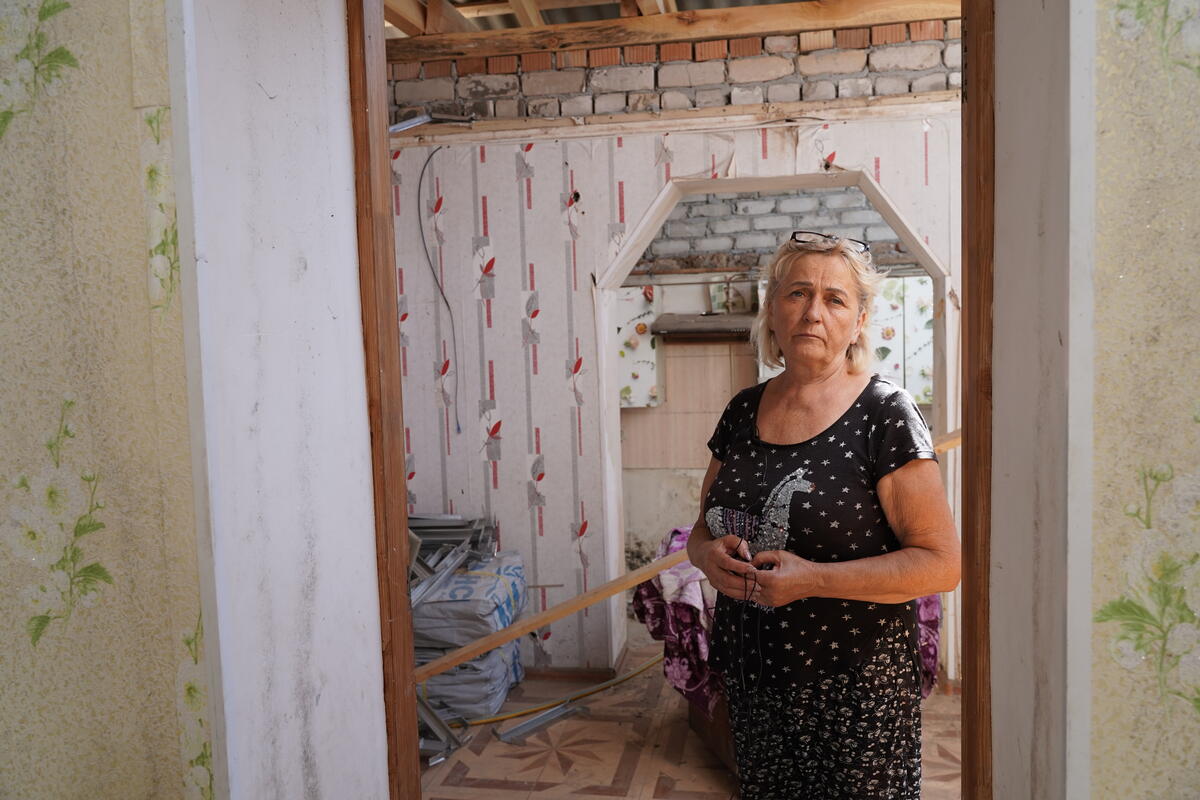 A woman stands in a damaged house.